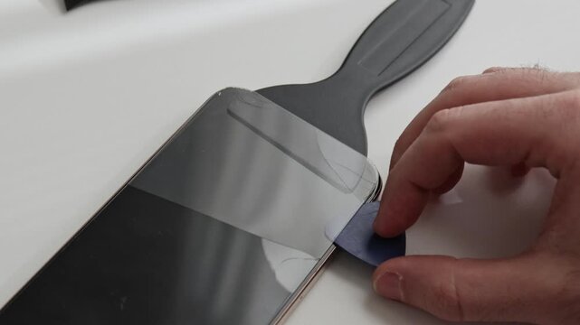 Man replaces cracked glass on phone screen at home. Hand removes broken glass, unpacks wipe, cleans dust and uses tools to install new glass. Repair process, close view, device maintenance.