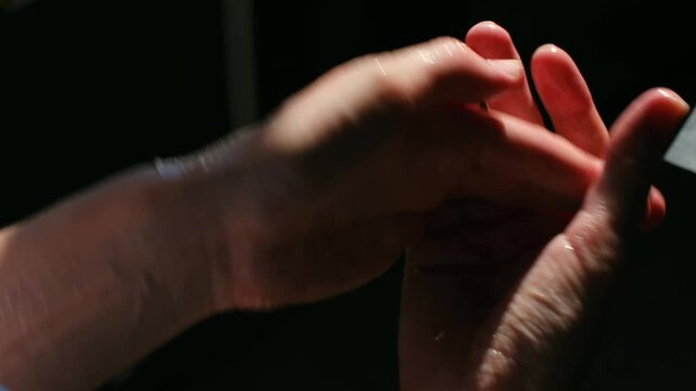 Close up person applying hydrating aloe vera cream, massaging lotion in her hands and fingers for soft, moisturized skin care, dark background in natural light. Applying aloe vera cream on hands