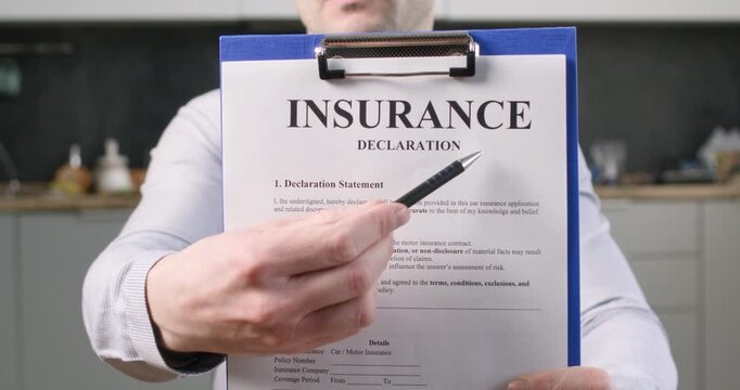 Man shows insurance declaration on clipboard pointing at contract text with pen.Driver highlights policy section explaining coverage details during document review
