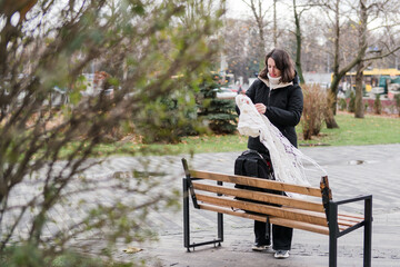 Fototapeta premium Caucasian woman in her 40s with dark hair wearing warm clothes walking on the street with her backpack and phone. Mature female spending time outdoors doing her routine tasks and breathing fresh air.