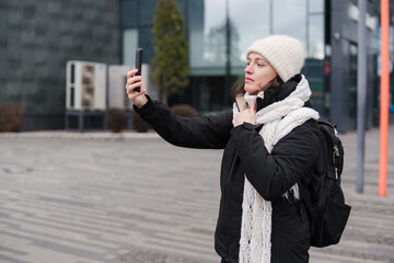 Fototapeta premium Caucasian woman in her 40s with dark hair wearing warm clothes walking on the street with her backpack and phone. Mature female spending time outdoors doing her routine tasks and breathing fresh air.