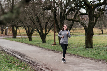 Fototapeta premium Caucasian woman in her 40s with dark hair wearing warm sport clothes doing exercises outdoors in autumn park. Mature female enjoying her personal time, jogging, stretching and breathing fresh air.