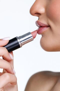 Beautiful calm tender girl with bare shoulders with lipstick in her right hand looks at her lipstick with a full lips