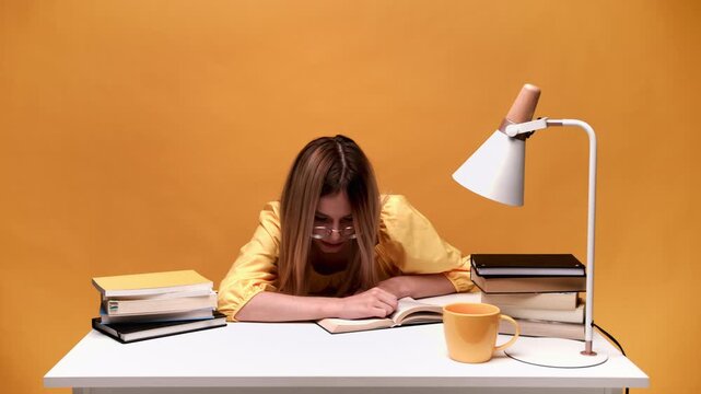Tired female student sleeping on a book at her desk waking up and continuing studying with fatigue and headache at night