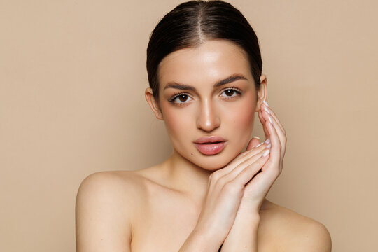 Skin care model. Beautiful young woman with perfect skin touching her face and posing against beige background.
