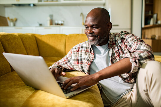 Smiling mature man using laptop on yellow sofa at home