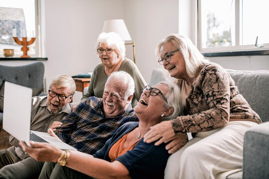 Senior friends laughing together with laptop in living room
