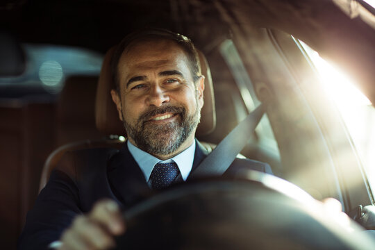 Smiling businessman driving car in sunlight