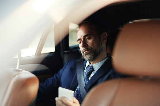Business executive using smartphone in car back seat