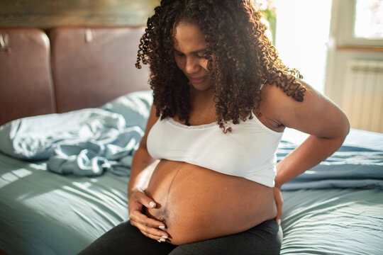 Pregnant woman with backache sitting on bed at home