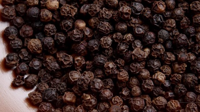 A pile of dried aromatic black peppercorns in a kitchen bowl. Rotation