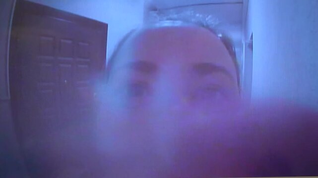 Woman trying to call through door peephole in apartment hallway.