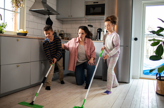Mother helping children mop kitchen floor at home