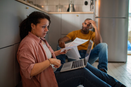 Worried couple reviewing bills on laptop in home kitchen