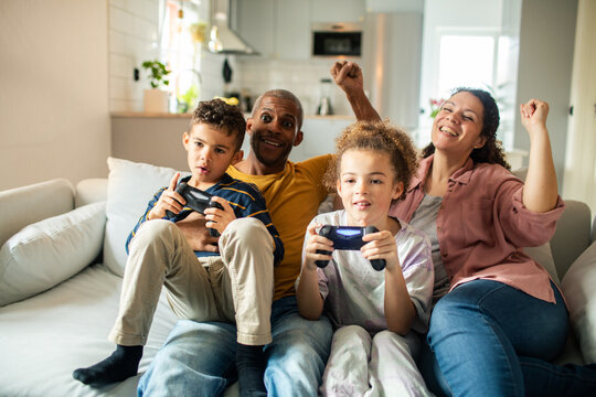 Parents cheering while kids play video games on couch at home