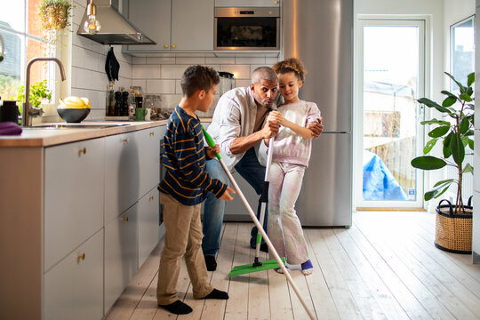 Father and children mopping kitchen floor at home
