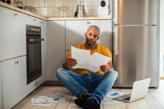 Concerned man reviewing household bills in kitchen