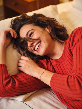 Gl&uuml;ckliche junge Frau mit Sommersprossen entspannt im Bett und l&auml;chelt in die Kamera