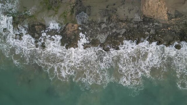 Aerial top down view of ocean waves crashing on rocky coastline