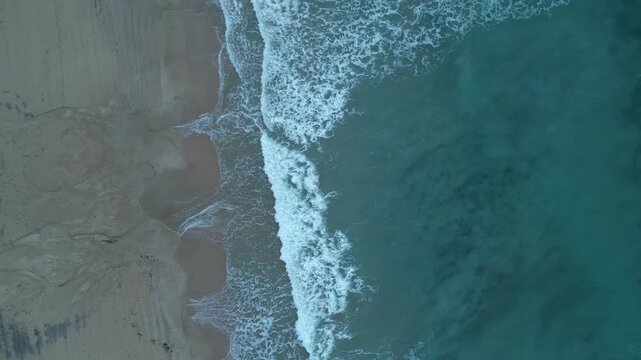Aerial top down view of ocean waves crashing on a sandy beach
