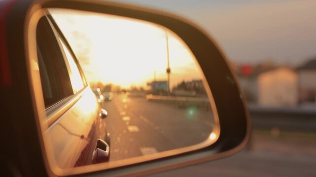The sun is reflected in the mirror, evening road. View in the side rear view mirror of a red car driving along the highway