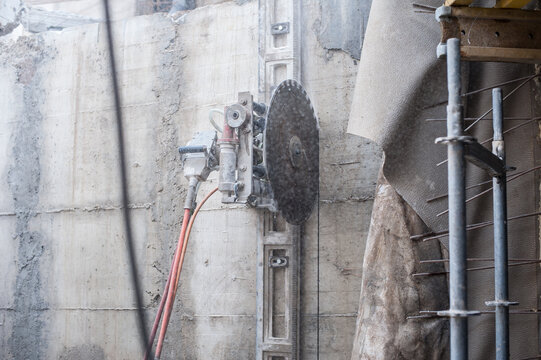 A wall cutter stands ready, its sharp blade poised against a concrete surface at a lively construction site. Dust swirls around as skilled workers prepare for the next phase of building