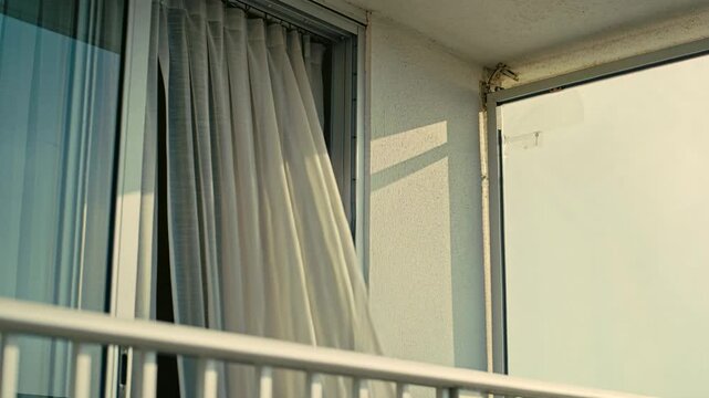 Billowing sheer white curtain moving outward on balcony railing as breeze lifting fabric settling