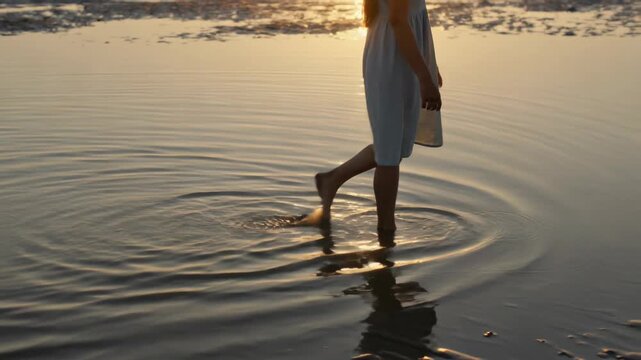 Walking teen in dress wading through tidal pool at sunset, low tide revealing ripples, bare feet