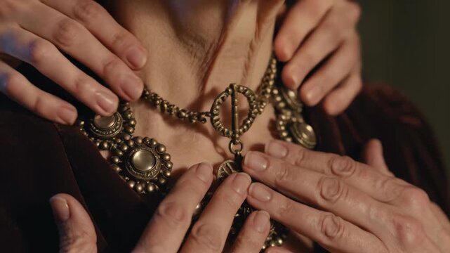 Reaching hands fastening necklace clasp on woman in burgundy gown in dressing room for event