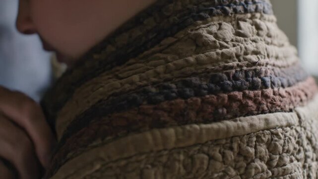 Feeling cool draft, senior's ringed aged hands tucking quilt around bare shoulder home by window