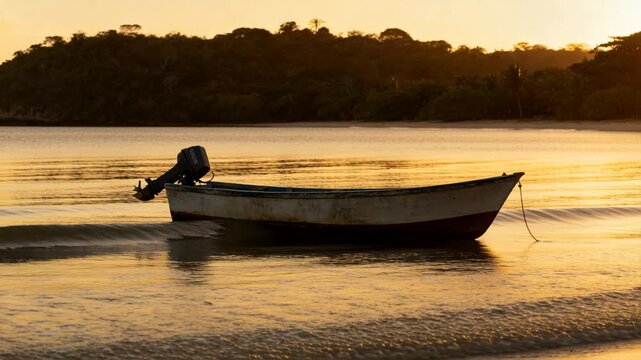 Incoming waves nudging skiff at shore, skiff rocking with outboard motor and golden wet sand