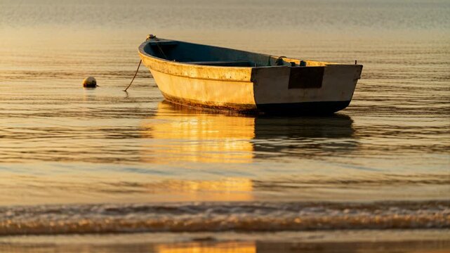 Bobbing weathered dinghy tethered to buoy at shallow shore, tide and wind creating small waves