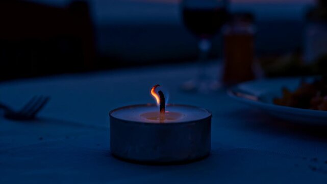 Tealight candle burning steadily on dining table, flickering then extinguishing, releasing smoke