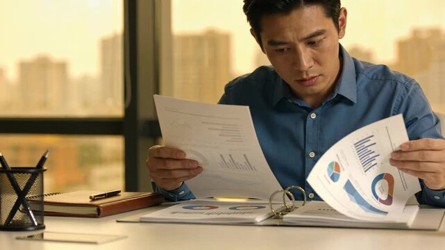 Lifting sheet, man in blue shirt studying charts in three-ring binder at desk, reviewing data