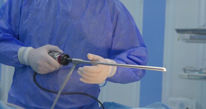 Professional surgeon in sterile blue scrubs holding a long laparoscopic trocar instrument during a minimally invasive surgery.