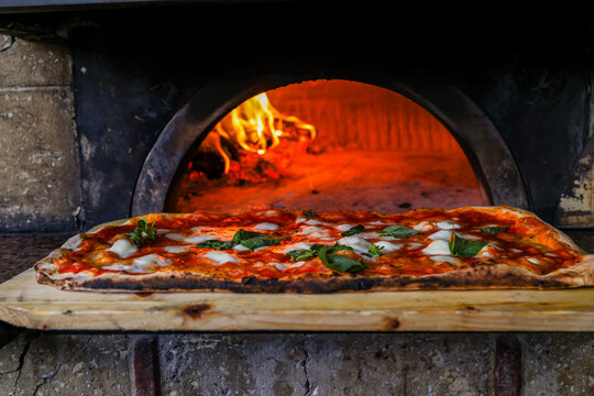 Pizza Margherita a metro tradizionale napoletana con sugo di pomodoro, mozzarella e basilico tenuta in caldo davanti al forno a legna acceso