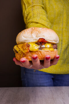 Panino ripieno di hamburger di carne, bacon croccante, provola affumicata e uovo a occhio di bue tenuto in mano da una cliente di una braceria 