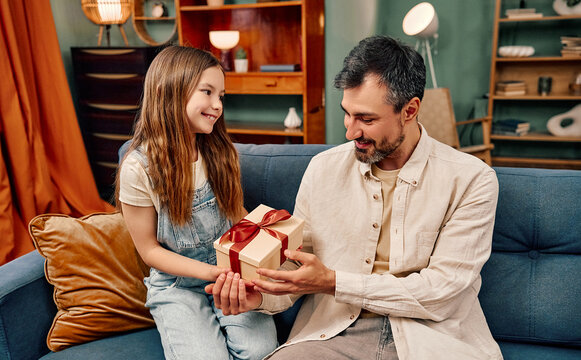 ather receiving gift from daughter on sofa at home