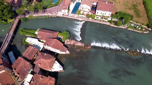 Italy Borghetto sul Mincio aerial drone top-down spiral over river houses and waterfalls. Medieval village mills and Mincio river cascades 4k travel destination Valeggio sul Mincio scenery