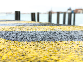 Obraz premium Wet yellow and black striped surface with blurred waterfront background