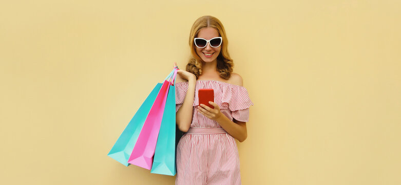 Beautiful happy young woman holding phone with colorful shopping bag on studio background