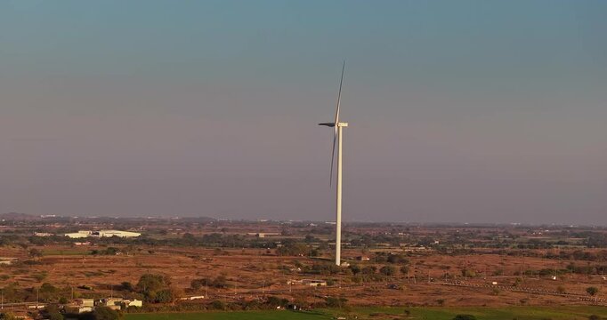 Golden hour aerial view of wind turbines across rural farmland, with rotating blades under a warm orange sky, showcasing clean energy and a serene countryside landscape of Gujrat, India