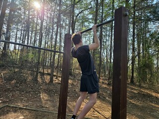 A young man engages in physical training and sports outdoors, performing pull-ups on an outdoor pull-up bar. The concept of outdoor recreation and sports.