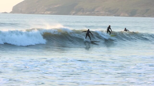 Pan of surfers catching waves in the surf mecca of Croyde in Devon at sunset, one of the best surf breaks in Europe