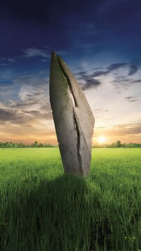 Tall, weathered stone monolith standing in a vibrant green grassy field at sunset rock