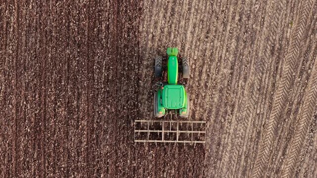 Crop field cultivation with green tractor and harrow, agronomy and agribusiness workflow. Farming machinery working soil preparation for planting season in rural agriculture. Tractor moving across