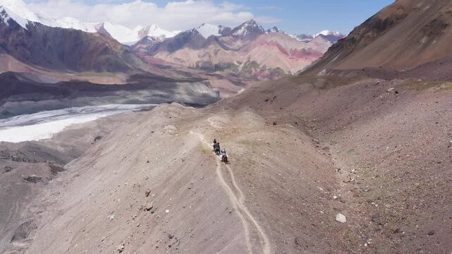 Aerial footage of picturesque wide angle Pamir mountains valley with small horsemen silhouettes heading by dusty mountain path carrying bags as local goods delivery service. Kyrgyzstan travel concept