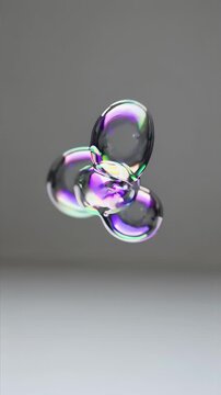 Close-up of iridescent soap bubbles arranged in a vertical stack; translucent spheres reflect rainbow colors on a soft gray background