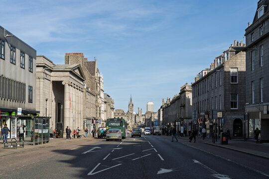 Aberdeen city center street vibrant with pedestrians, vehicles, and historic granite architecture under bright blue sky