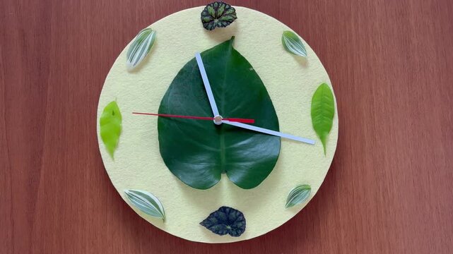 Time of spring. Video of handmade clock with a yellow dial, decorated with green young leaves instead of numbers, on a wooden background. Concept for the arrival of spring